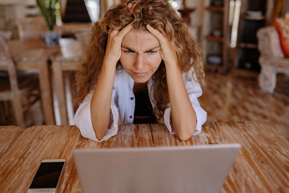 A photo of a frowning woman sitting at a desk and looking at her computer, with her hands in her hair.