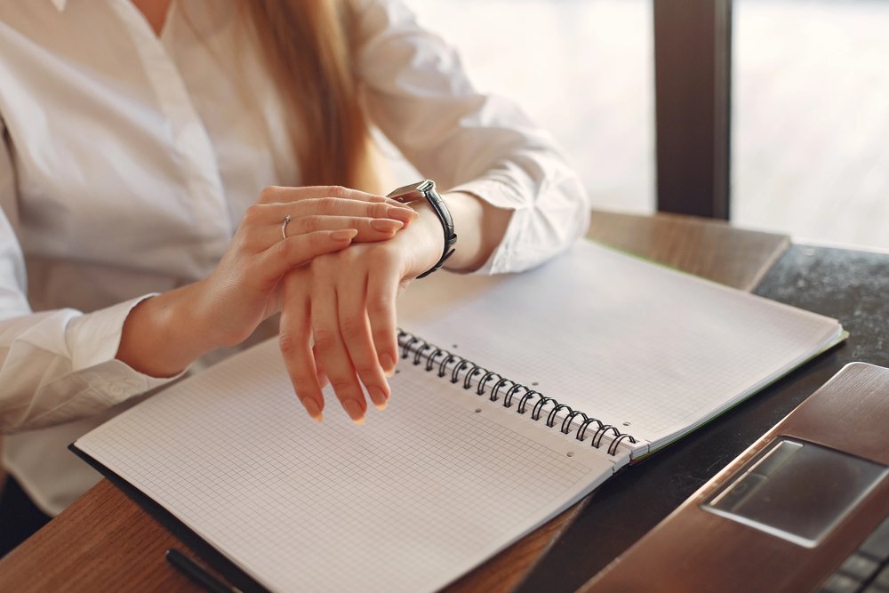 A photo sitting at a desk looking at her watch.