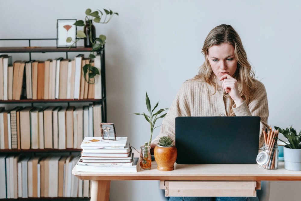 A woman sitting in an airy study reading on her laptop.